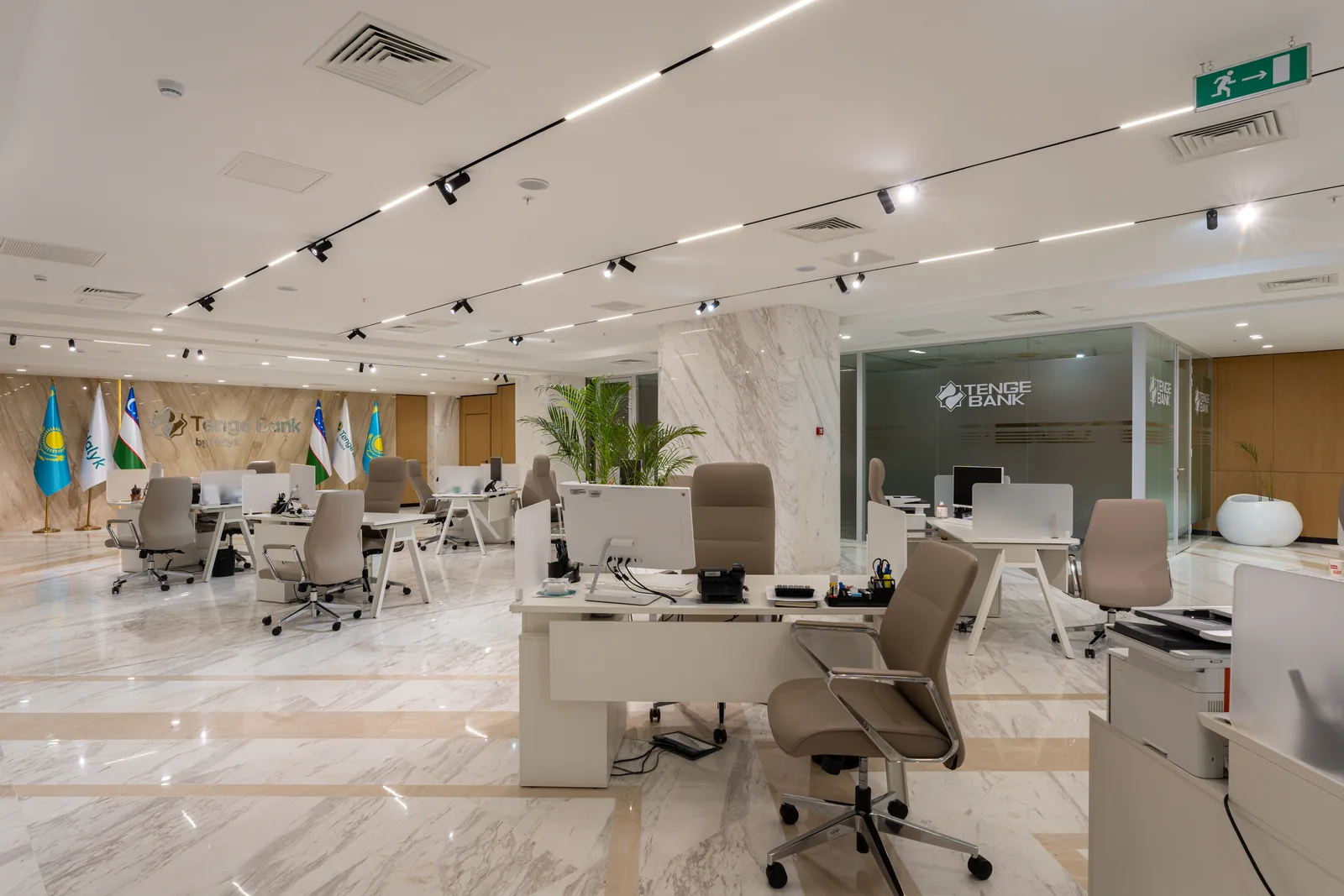 Open space Tenge Bank: белые столы, бежевые кресла, флаги и логотип банка на стене и на стеклянной перегородке