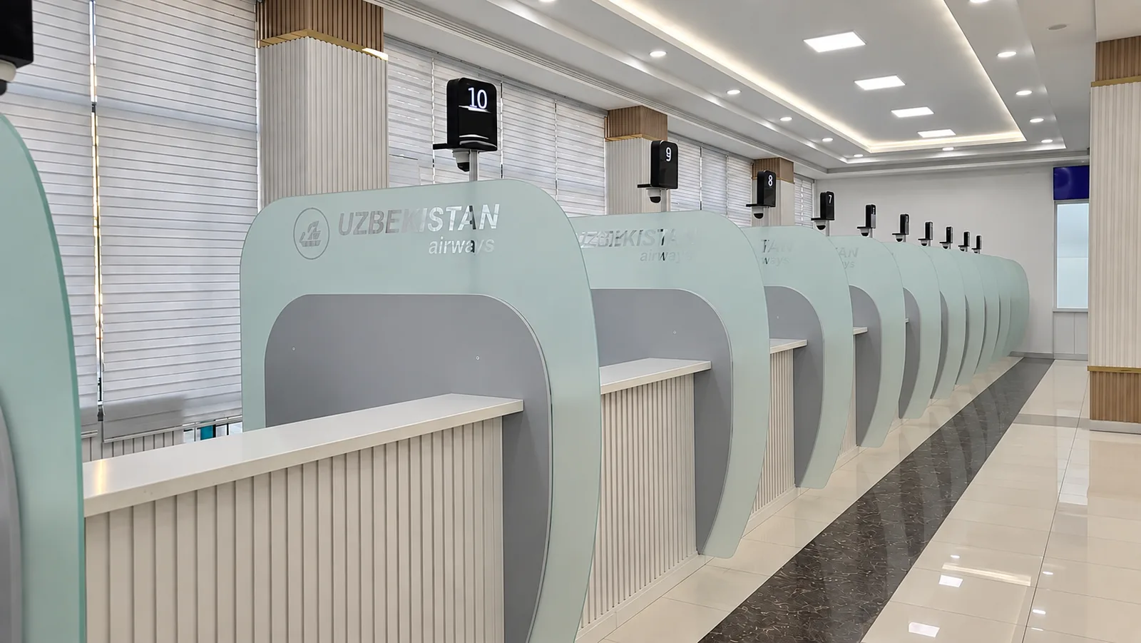 Ряд окон обслуживания Uzbekistan Airways: стойки с матовыми перегородками с логотипом авиакомпании и номера окон